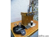 The image shows a wooden bar counter with a Guinness beer dispenser on it. The dispenser is made of wood and has four taps on...