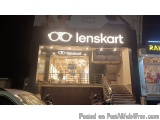 The image shows the entrance of a Lenskart store at night. The store is located on a street corner with a car parked in front...