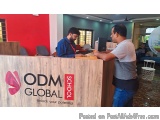 The image shows two men standing behind a wooden reception desk with the logo of ODM Global School on it. The desk is located...