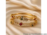 The image is a close-up of a gold bangle bracelet. The bracelet is made of gold and has a floral design with intricate detail...