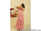 The image shows a young girl standing in front of a white wall with a bouquet of flowers on the left side. She is wearing a l...