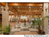 The image shows the interior of a luxurious hotel lobby. The lobby has a high ceiling with wooden beams and a large wooden pe...