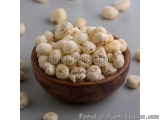 The image shows a wooden bowl filled with small, round, white nuts. The nuts appear to be whole and have a light brown color....