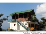 The image shows a two-story house with a green roof. The house has a white exterior with a red door and a balcony on the seco...