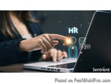 The image shows a person's hand pointing towards a laptop screen. The laptop is placed on a wooden table and the background i...