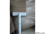 The image shows a close-up of a white vacuum cleaner nozzle attached to a beige fabric. The nozzle is long and cylindrical in...
