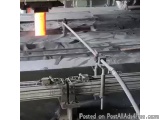 The image shows a large industrial machine with a long metal rod attached to it. The rod is being used to cut a piece of meta...