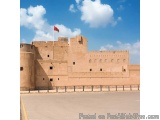 The image shows a large, ancient castle with a red flag flying on top of it. The castle is made of sandstone and has multiple...