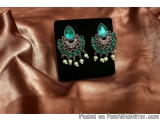 The image shows a pair of earrings on a black velvet background. The earrings are in the shape of a teardrop and have a green...