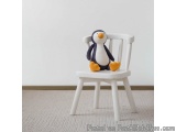 The image shows a small white wooden chair with a stuffed penguin sitting on it. The chair has four legs and a curved backres...