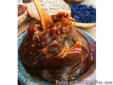 The image shows a close-up of a dish in a blue bowl. The dish appears to be a type of meat, possibly beef or pork, with a dar...