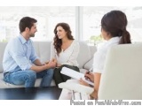 The image shows a man and a woman sitting on a couch in a living room, engaged in a conversation. The man is on the left side...