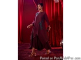 The image shows a young woman walking on a red carpeted stage with a red curtain in the background. She is wearing a long, fl...