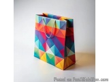 The image is of a colorful shopping bag made from paper. The bag is rectangular in shape and has a handle on the top for easy...