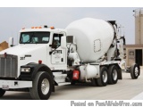 The image shows a large white cement mixer truck parked on a concrete surface. The truck has a large tank on the back and a f...