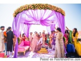 The image shows a traditional Indian wedding ceremony taking place outdoors. The focal point of the image is a large arch dec...