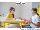 The image shows a young girl sitting at a yellow table with a young woman sitting next to her. The girl is wearing a white po...