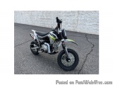 The image shows a dirt bike parked on a concrete surface. The bike is black and white with a green and yellow stripe on the s...