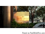 The image shows a signboard with the text "M&M Golf Hills" written in gold letters. The signboard is located in front of a bu...