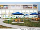 The image shows the exterior of a Tata Motors dealership. The dealership is a large building with a white facade and multiple...