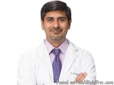 The image is a professional headshot of a man named Dr. Sachin. He is wearing a white lab coat with a purple tie and a pink c...