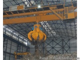 The image shows a large yellow crane in a warehouse. The crane has a long arm with a hook at the end, which is used to lift a...