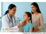The image shows a young girl sitting in a hospital room with her mother and nurse. The girl is wearing a blue t-shirt and has...