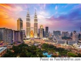 The image is a panoramic view of the city of Kuala Lumpur, Malaysia. The sky is a beautiful orange and pink color, with the s...