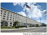 The image shows a large, modern building with a flat roof and multiple windows. The building is located on a street corner wi...