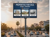 The image shows a large blue billboard on the side of a road. The billboard is advertising properties for sale in Zundal, Ahm...