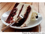 The image shows a slice of cake on a white plate with a fork. The cake appears to be a layered cake with layers of white fros...
