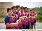 The image shows a group of young boys standing in a line with their arms crossed. They are all wearing blue and red sports je...