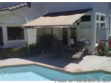 The image shows a beautiful backyard of a house with a swimming pool. The house has a white exterior with a tiled roof and la...
