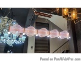 The image shows a modern chandelier hanging from the ceiling in a room. The light fixture is made of metal and has a pink and...