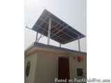 The image shows a building with a large solar panel on top of it. The solar panel is mounted on a metal frame and is supporte...
