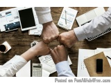 The image shows two people shaking hands over a desk with various office supplies scattered around. The desk is made of wood...