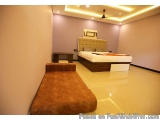 The image shows a modern and minimalist bedroom with a large bed in the center. The bed has a beige headboard and white linen...