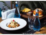 The image shows a table setting with a plate of food and two bottles of water. The plate is white and has a salad on it. The...
