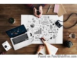 The image shows a desk with a laptop, a notebook, a camera, a plant, and other office supplies scattered around. On the desk,...
