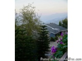 The image shows a view of a residential area with a mountain range in the background. The sky is overcast and the overall moo...