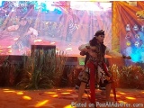 The image shows a stage with a large screen in the background. On the stage, there are two dancers performing a traditional d...