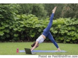 The image shows a young woman performing a yoga pose on a blue mat in a garden. She is wearing a white tank top and blue legg...