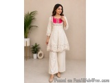 The image shows a young woman wearing a traditional Indian outfit. She is standing in a room with a beige background and a po...