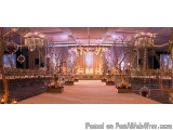 The image shows a large, elegant wedding venue with a high ceiling and white walls. The floor is covered with a white carpet...