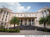 The image shows a large, two-story building with a beige exterior and white columns. The building has a large entrance with a...