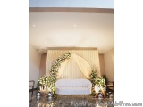 The image shows a beautiful and elegant wedding stage setup. The stage is decorated with a white sofa in the center, surround...
