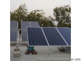 The image shows a group of solar panels installed on a rooftop. The panels are arranged in a grid-like pattern and are suppor...