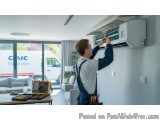 In this image, we can see a man working on an air conditioning unit in a modern living room. He is wearing a blue overalls an...