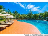 The image shows a large swimming pool with crystal clear blue water. The pool is surrounded by a tiled floor and there are se...