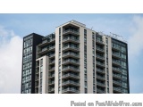 The image shows a tall, modern building with multiple floors and balconies. The building appears to be made of glass and stee...